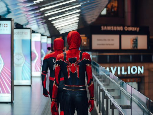 Two cosplayers dressed as Spider-Man walk through a brightly lit shopping mall in Kuala Lumpur.